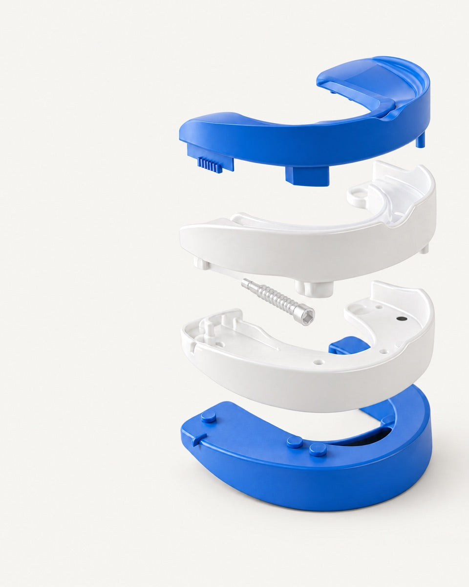 The mouthguard taken apart into four stacked pieces: a blue upper layer, a white upper tray, a white lower tray and a blue lower layer, with the adjustment screw between them.