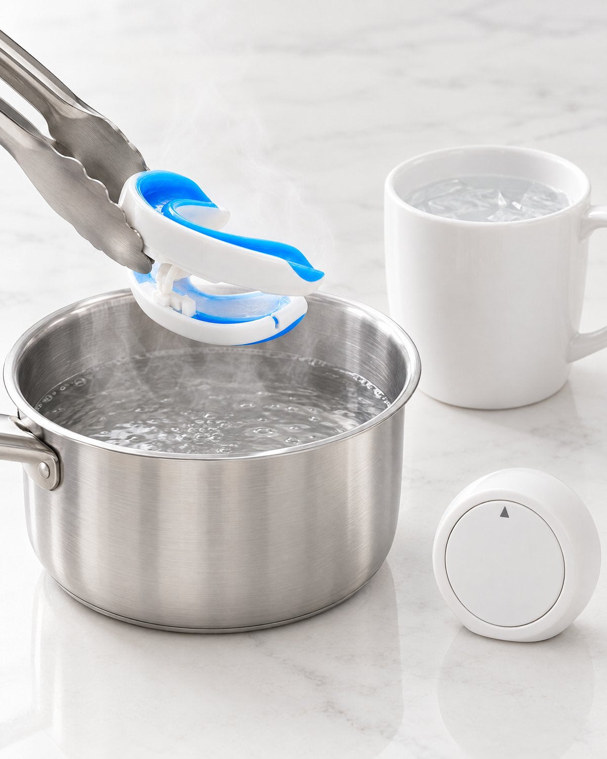 Kitchen still life for the molding step: a pot of steaming water, kitchen tongs holding the mouthguard above it, a mug of cold water and a plain white timer.