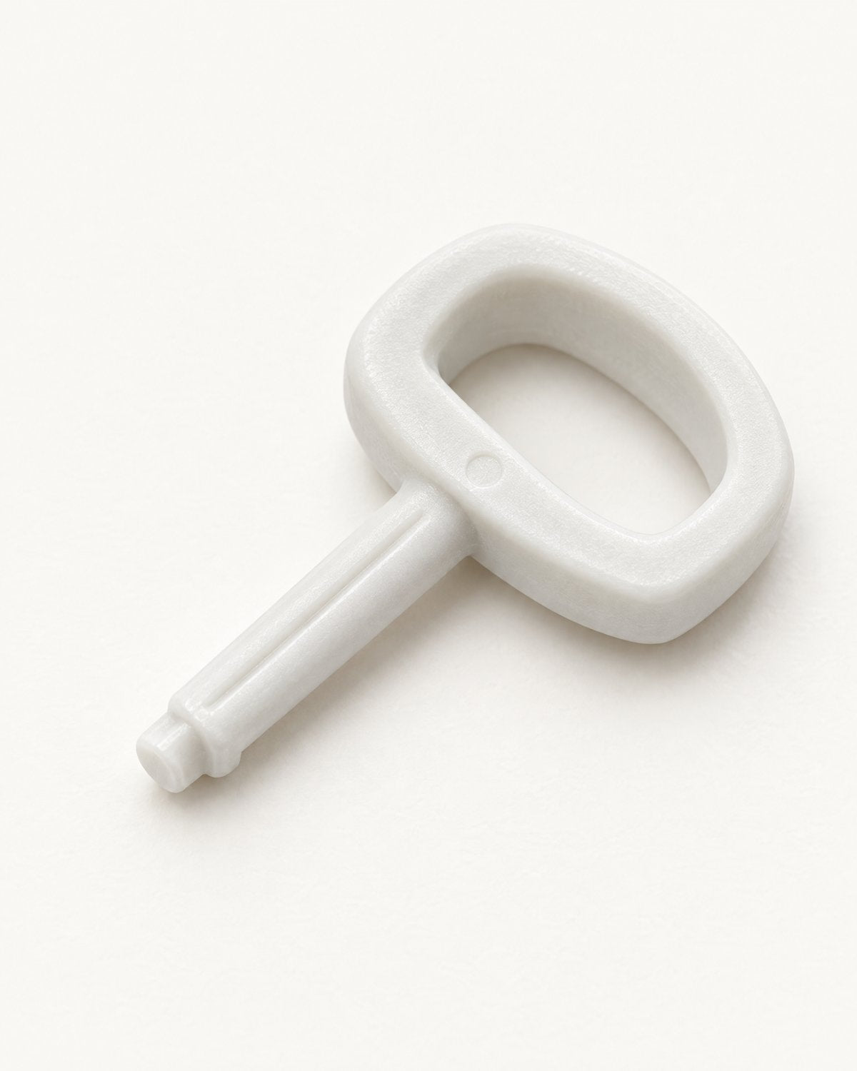 The small white calibration key on a porcelain surface, with its D-shaped loop handle and short shaft.